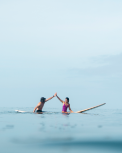Two friends surfing while high fiving